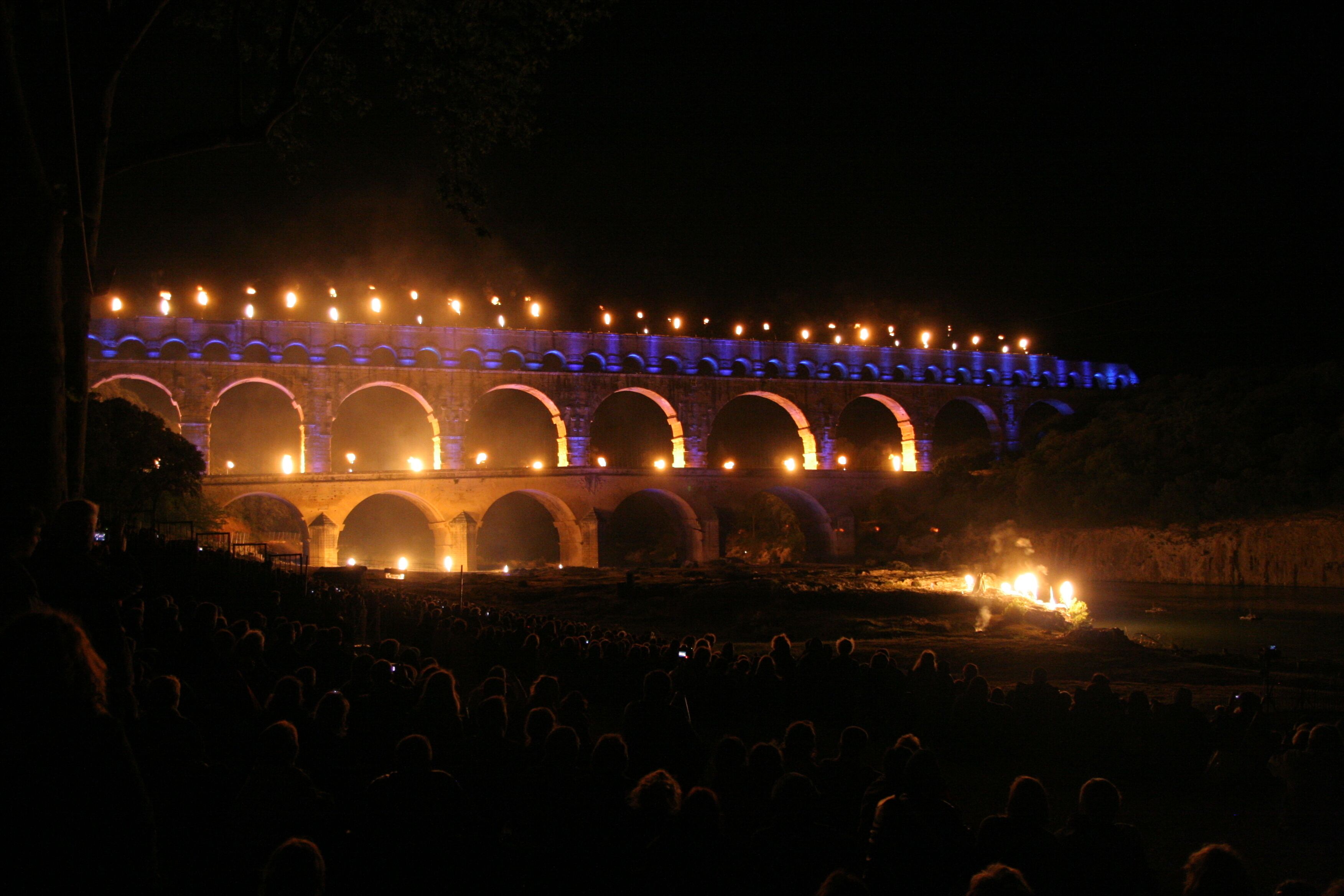A large, illuminated bridge with multiple arches, surrounded by a crowd of people.