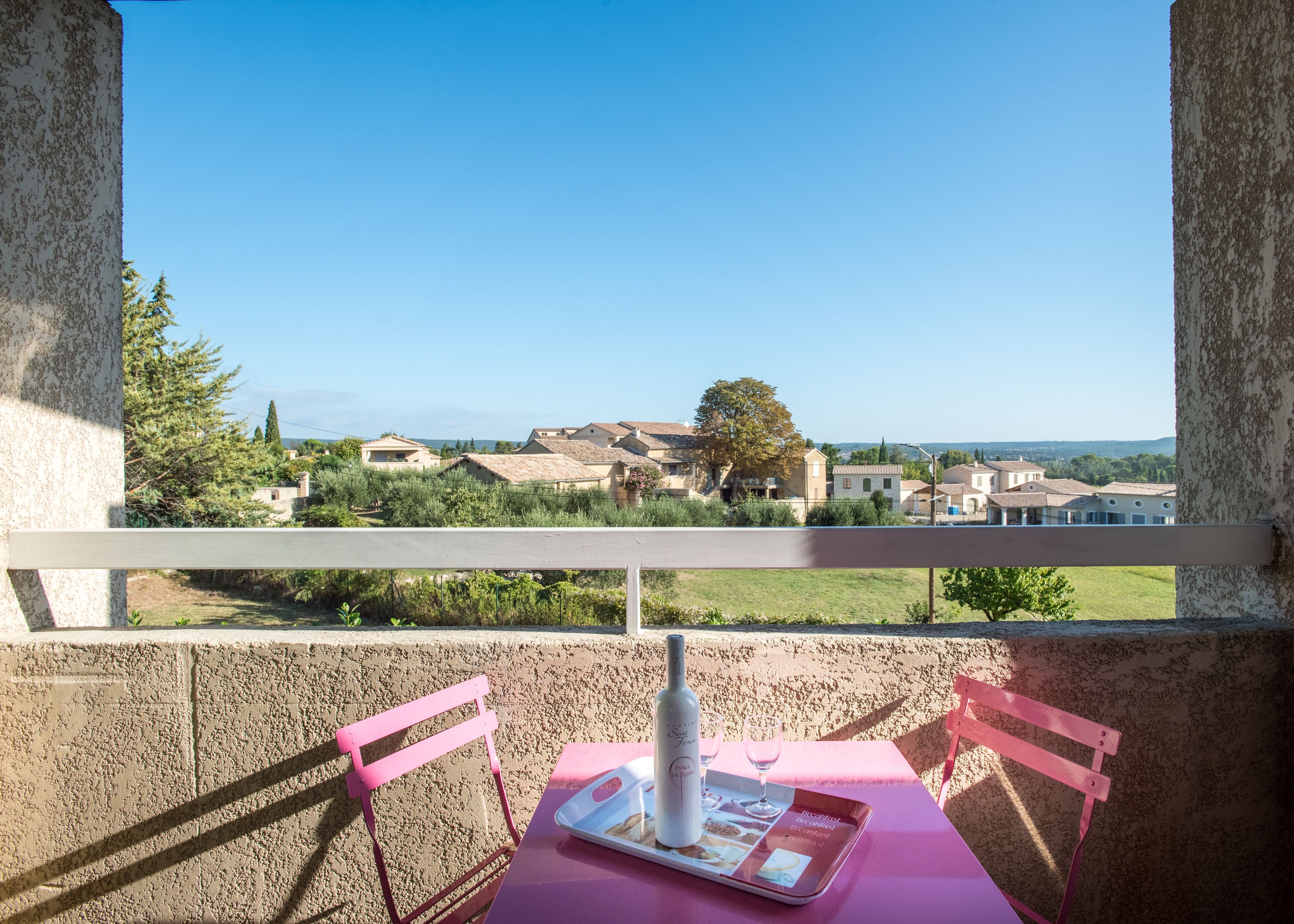 Ein Balkon mit Tisch und Stühlen, mit Blick auf ein Dorf mit Häusern und Grünflächen.