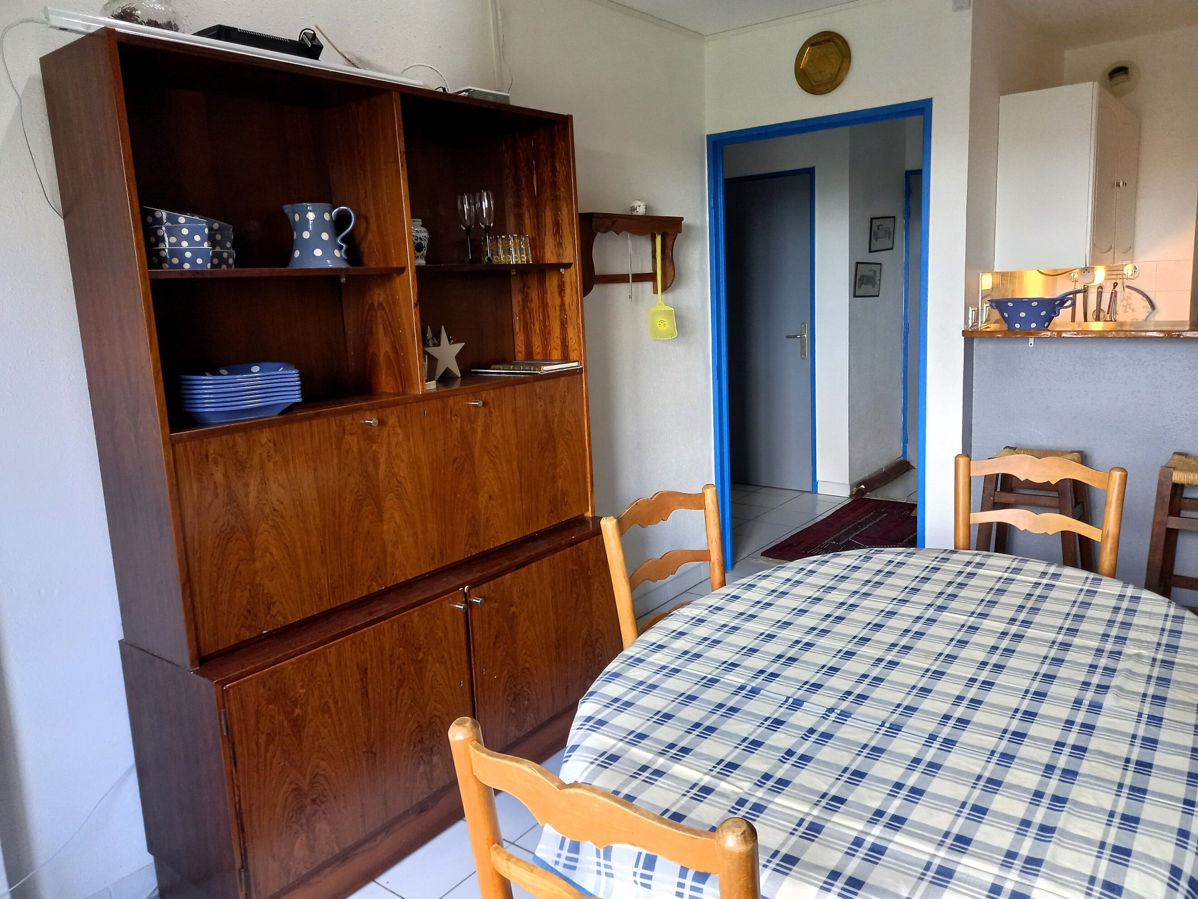 A dining area with a wooden cabinet, a table with a checkered tablecloth, and chairs.
