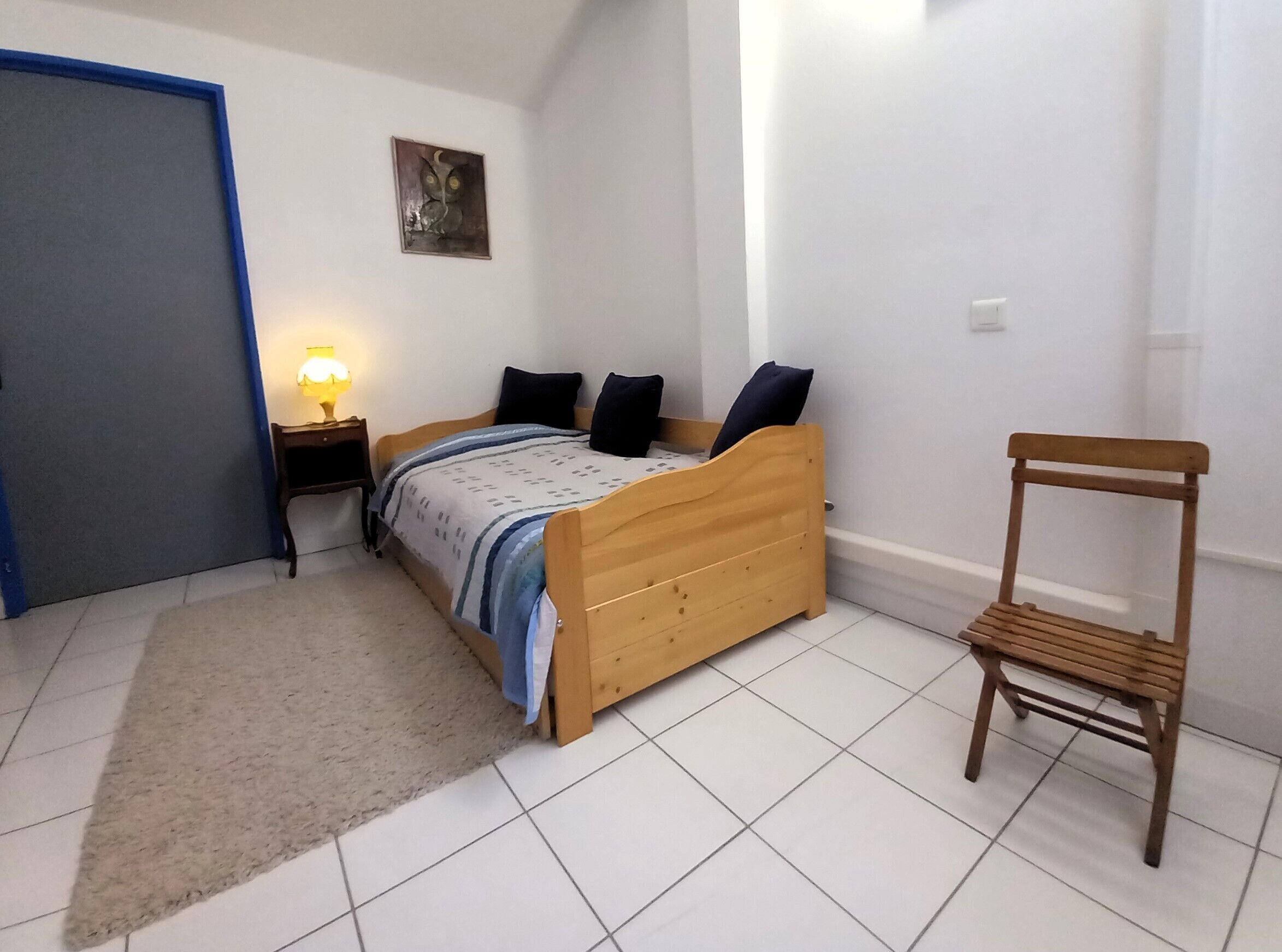 Una camera da letto con un letto di legno, un comodino, una sedia, un tappeto e un quadro appeso al muro.