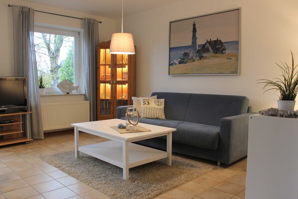 A living room with a grey sofa, white coffee table, and a painting of a lighthouse.