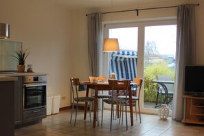 A kitchen with an oven, a dining table with chairs, a TV stand, and a view of the outdoors through a glass door.