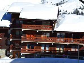 Un edificio de madera de varios pisos con balcones, rodeado de laderas nevadas.