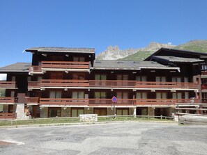 A multi-story hotel with wooden balconies and a stone facade, set against a mountainous backdrop.