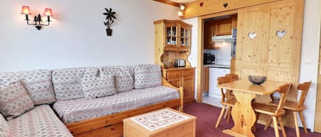 A cozy living room with a patterned sofa, a wooden coffee table, and a dining area with a wooden table and chairs.