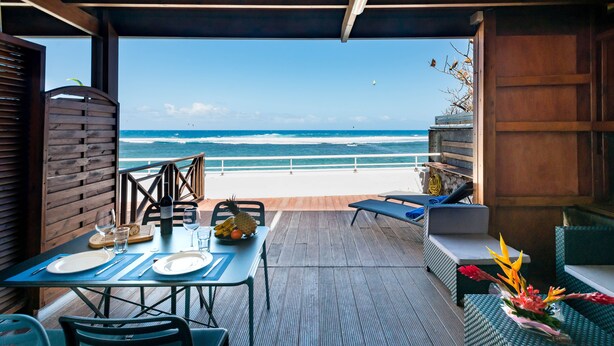 A dining area with a view of the ocean, featuring a table set with plates, cutlery, and a fruit bowl. - REVE AUSTRAL T2 C au bord du Lagon 180° sea view (St Pierre)