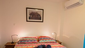 A bedroom with a colorful bedspread, a framed picture on the wall, and an air conditioning unit. - REVE AUSTRAL T2 C au bord du Lagon 180° sea view (St Pierre)
