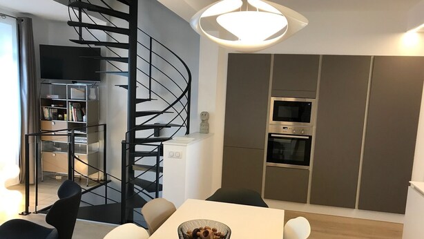 A modern kitchen with built-in appliances, a dining area with a white table and chairs, and a spiral staircase leading to an upper level. - DUPLEX IN BEAUTIFUL TOUQUETTOISE, PROX. SHOPS & ST. JEAN STREET, 150M SEA FRONT (Le Touquet-Paris-Plage)