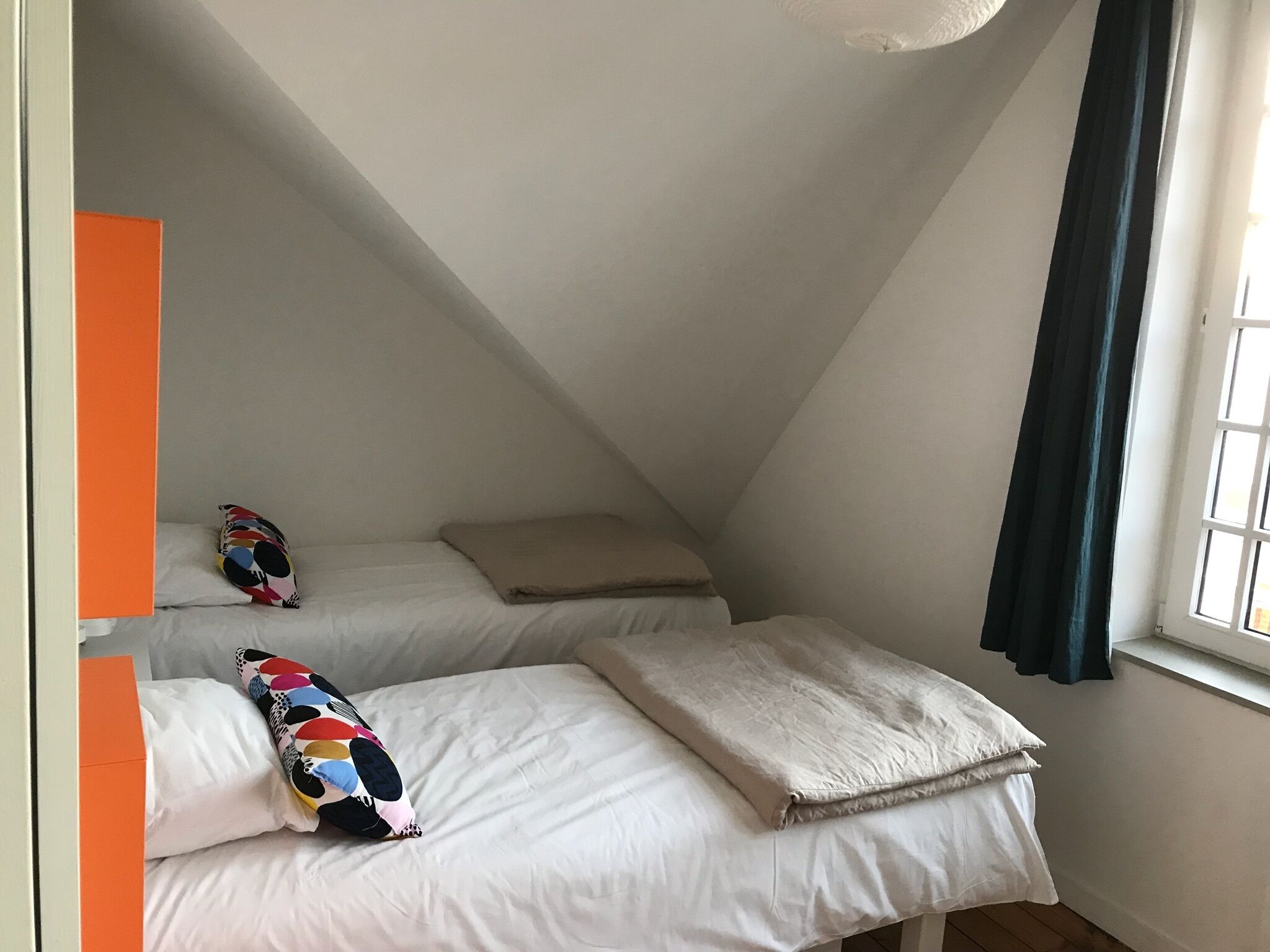 Um quarto de sótão pequeno e triangular com duas camas, cada uma com travesseiro e manta colorida.