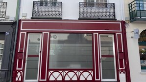 A two-story building with a white facade and red trim. It features two windows on the upper floor and a large garage door on the ground floor. - DUPLEX IN BEAUTIFUL TOUQUETTOISE, PROX. SHOPS & ST. JEAN STREET, 150M SEA FRONT (Le Touquet-Paris-Plage)