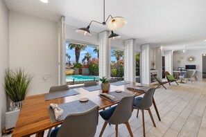 Un comedor con mesa de madera, sillas y vistas a una piscina.