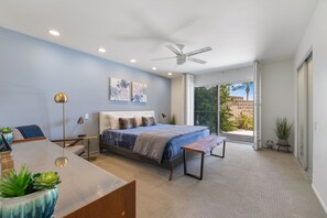 Un dormitorio moderno con cama, mesitas de noche, un escritorio y un balcón con vistas a zonas verdes.