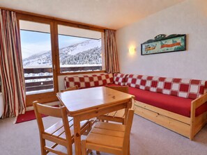 Una stanza accogliente con un tavolo e sedie in legno, una panca a quadri rossi e bianchi, una finestra con vista su una montagna innevata e un cartello appeso al muro.