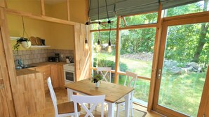 Une cuisine avec des meubles en bois, une table à manger avec des chaises, et une vue sur un jardin grâce à de grandes fenêtres.