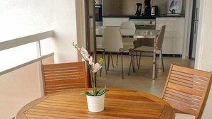 Un balcón con una mesa y sillas de madera, una orquídea en maceta y vistas a una zona de cocina.