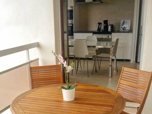 A balcony with a wooden table and chairs, a potted orchid, and a view of a kitchen area. - Appartment 55m² with sea view terrace 200m Calvi b (Calvi)