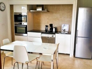 Une cuisine de taille réduite comprenant une table à manger, des chaises, un réfrigérateur et une machine à café.