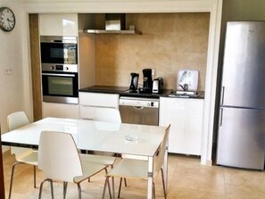 A modern kitchen with a dining table, chairs, a refrigerator, and a coffee maker.