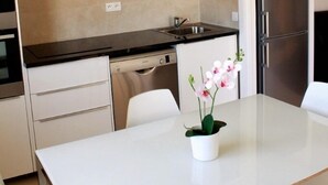 Cocina moderna con lavavajillas, pileta y refrigerador de acero inoxidable. Hay una mesa blanca con una orquídea en maceta.
