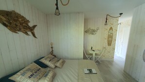 Een kamer met een bed, een bureau en een stoel. Er hangt een visdecoratie aan de muur en er staat een surfboard.