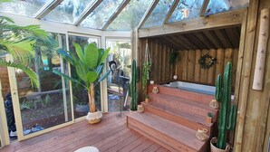 Een tuinkamer met houten traptreden naar een zithoek, omringd door verschillende planten en een glazen dak.