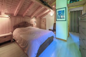 Una camera da letto con una testiera in legno, un letto con copripiumino bianco, un comodino, una lampada e una cassettiera.