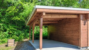 Une structure en bois couverte, dotée d’un plancher en béton et entourée d’un feuillage verdoyant et dense.