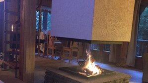 Un foyer en pierre dans une pièce en bois dotée d’un haut plafond et d’une grande fenêtre.