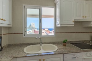 A kitchen with a double sink, a window with a view of buildings and a mountain, and white cabinets with gold handles.
