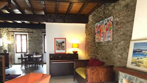 Un accogliente soggiorno con parete in pietra, divano in legno, zona pranzo con tavolo e sedie e camino sormontato da un quadro incorniciato.