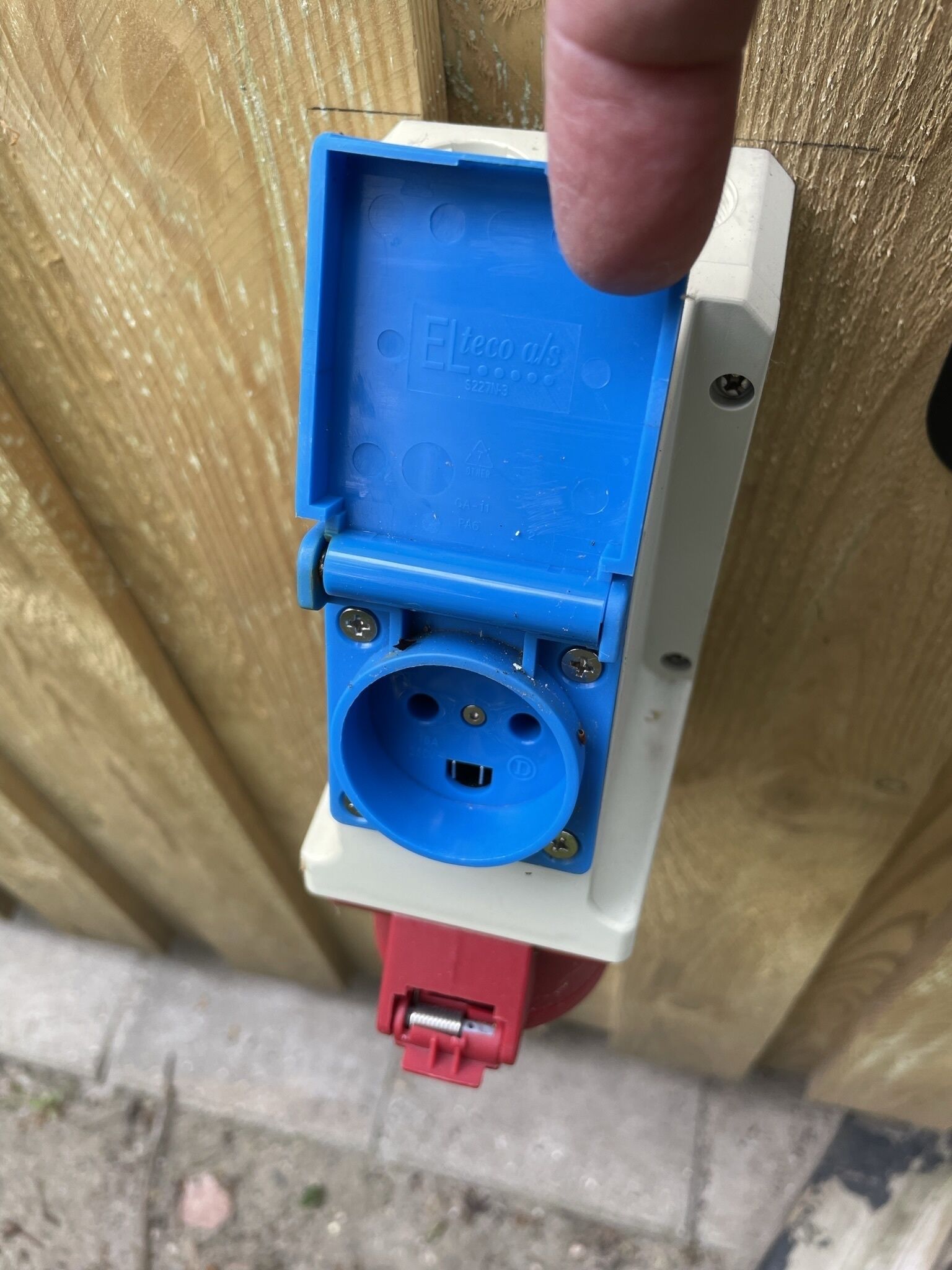 A close-up of a blue electrical plug with a red connector, mounted on a wooden surface.