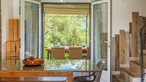A dining area with a glass table, wicker chairs, and a view of a garden through a glass door. - 2 villas with swimming pool in an olive grove in Corsica - near Saint-Florent (Oletta)