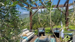An outdoor seating area with wicker furniture, a wooden pergola, and a view of the countryside. - 2 villas with swimming pool in an olive grove in Corsica - near Saint-Florent (Oletta)