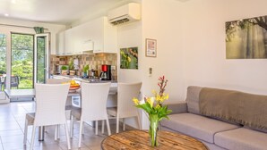 A modern kitchen with white cabinets, a dining area with wicker chairs, a round wooden table, and a grey sofa. - 2 villas with swimming pool in an olive grove in Corsica - near Saint-Florent (Oletta)
