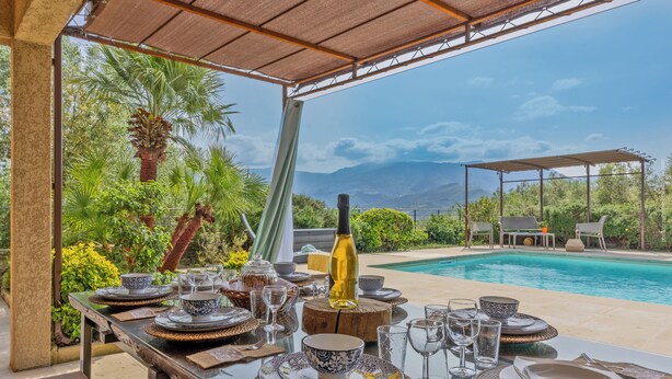 An outdoor dining area with a table set for a meal, overlooking a pool and a mountainous landscape. - 2 villas with swimming pool in an olive grove in Corsica - near Saint-Florent (Oletta)