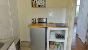 Una cocina compacta equipada con refrigerador, tostadora, hervidor y un estante con utensilios de cocina.