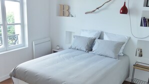 Un dormitorio con cama, lámpara colgante, mesita de noche, estante y una repisa con libros.