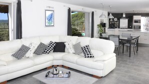 A modern living room with a white sectional sofa, a coffee table, and a dining area with a kitchen in the background. - beautiful house in olive grove, infinty pool and hot tub, panoramic view 8 pax (Callas)