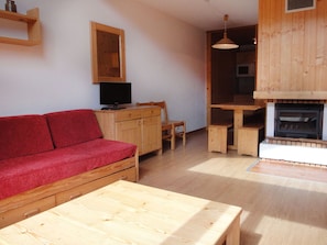 A cozy living room with a red sofa, wooden furniture, a television, and a fireplace.