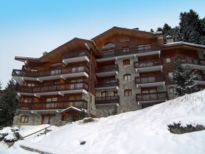 Un hotel de varios pisos con balcones, fachada de piedra y alrededores cubiertos de nieve.