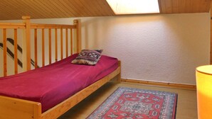 Une petite chambre avec un lit simple, un plafond en pente et un puits de lumière.