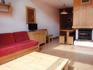 A cozy living room with a red sofa, wooden furniture, a television, and a fireplace.
