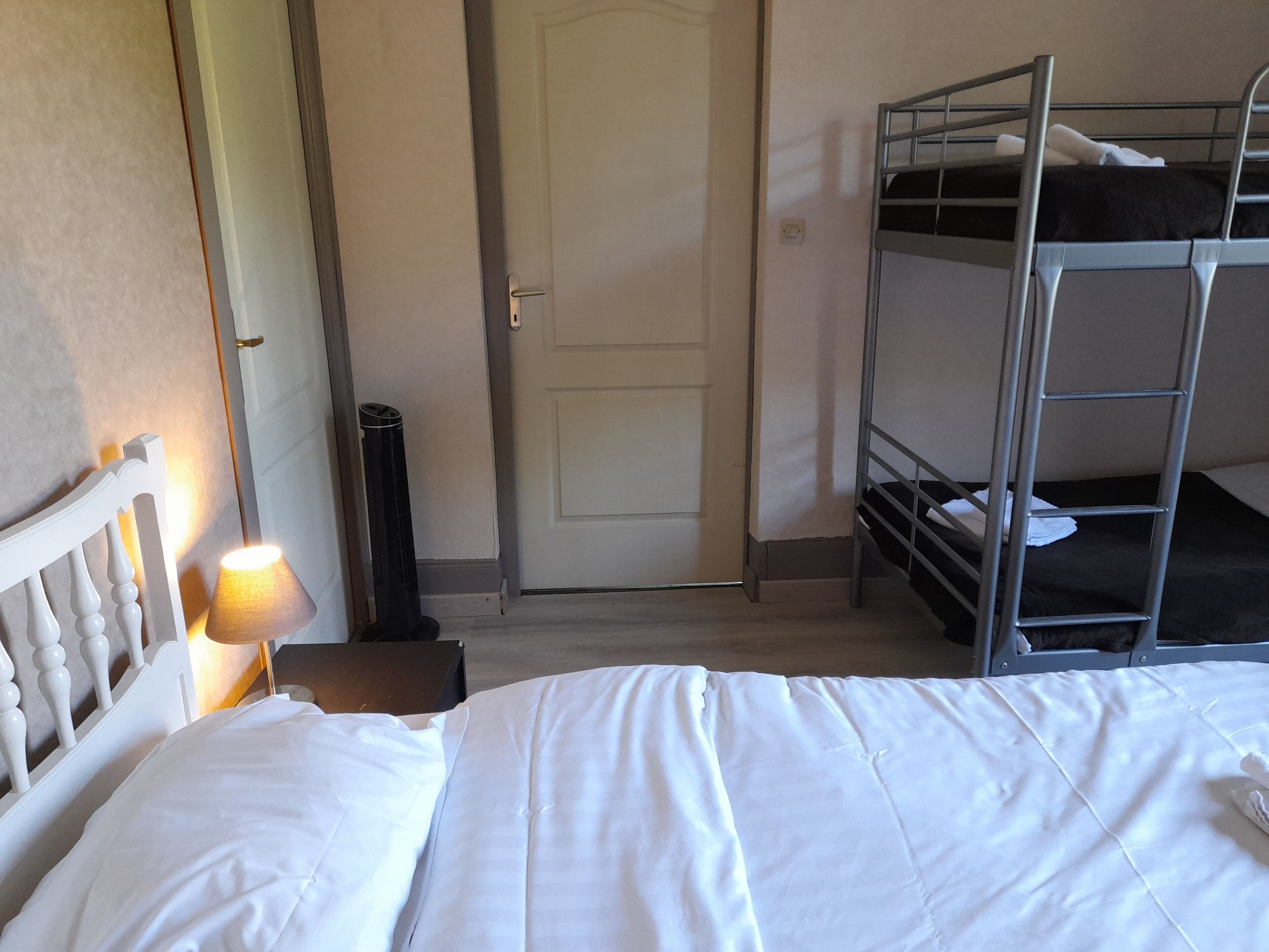Una camera d'albergo con un letto a castello, un letto singolo, una lampada e una porta.