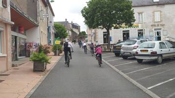 A street with cyclists, parked cars, and buildings including a hotel.
