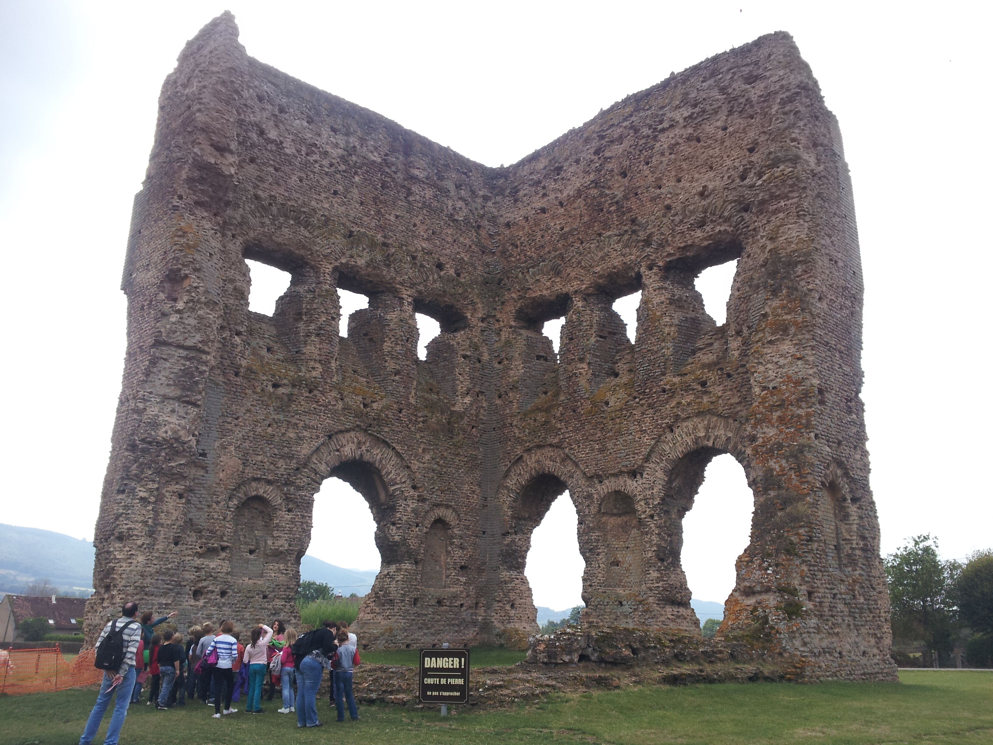 A large, ancient stone structure with multiple arches and a warning sign indicating danger due to falling rocks.