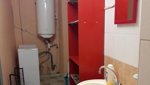 Une petite salle de bain avec un lavabo blanc, des rangements rouges, un radiateur blanc et un sol carrelé.