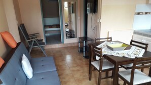 Un espace de vie comprenant un canapé, une table à manger, des chaises et un coin cuisine avec un téléviseur.