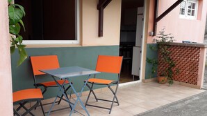 Un espace extérieur aménagé avec une table et quatre chaises orange, un pot de fleurs et une caméra de surveillance fixée au mur.