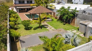 Una casa moderna con piscina, terraza cubierta y jardín exuberante.
