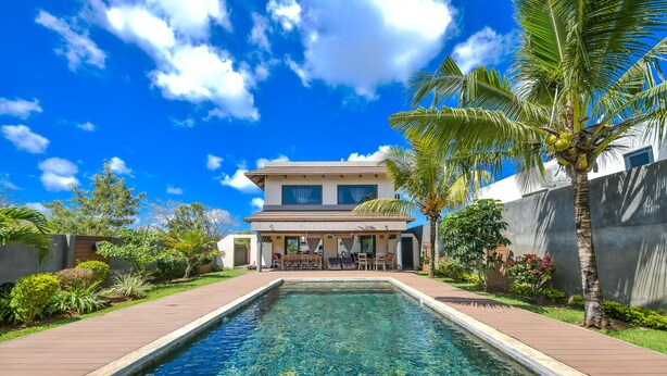 Una casa moderna con piscina, rodeada de exuberante vegetación y palmeras.